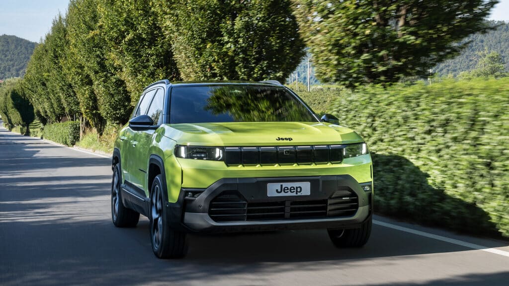 Auf diesem Bild ist ein leuchtend grüner Jeep Compass SUV zu sehen, der auf einer von Bäumen gesäumten Straße fährt.
