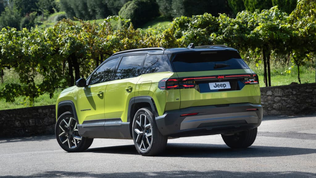 Auf diesem Bild ist ein leuchtend grüner Jeep Compass SUV von hinten schräg vor einer grünen Landschaft mit Bäumen und einer Steinmauer zu sehen.