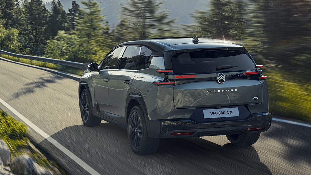 Auf diesem Bild ist ein dunkelgrauer Citroën C5 Aircross von hinten zu sehen, der auf einer kurvenreichen Straße durch eine bewaldete Berglandschaft fährt.