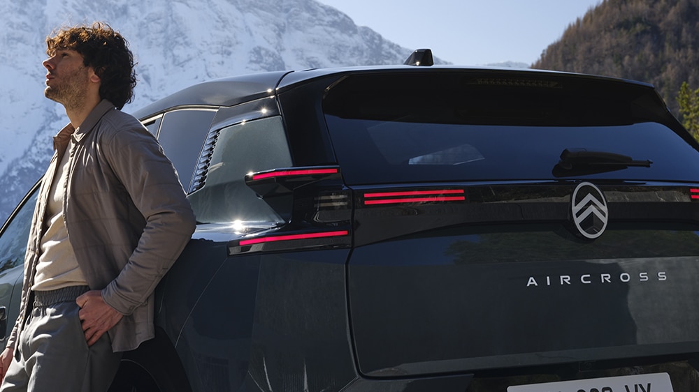 Das Bild zeigt einen Mann, der an einem dunklen Citroën Aircross SUV in einer winterlichen Berglandschaft lehnt.