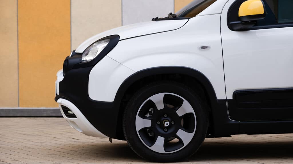 Auf diesem Bild ist ein weißes Fiat Pandina mit schwarzen Kunststoffverkleidungen und einem gelben Außenspiegel zu sehen.