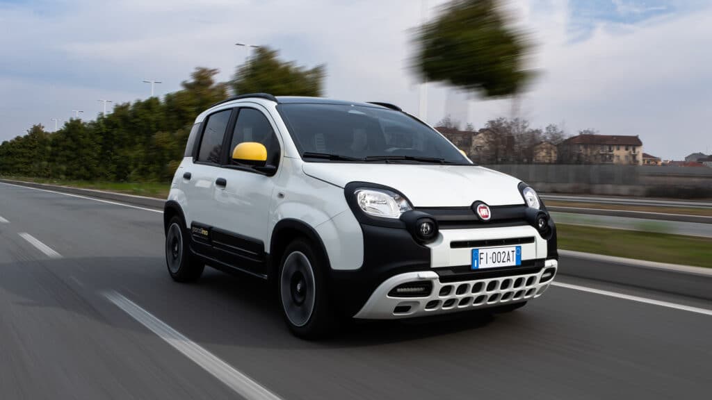 Auf diesem Bild ist ein weißer Fiat Pandina mit gelben Außenspiegeln zu sehen, der auf einer Straße fährt.