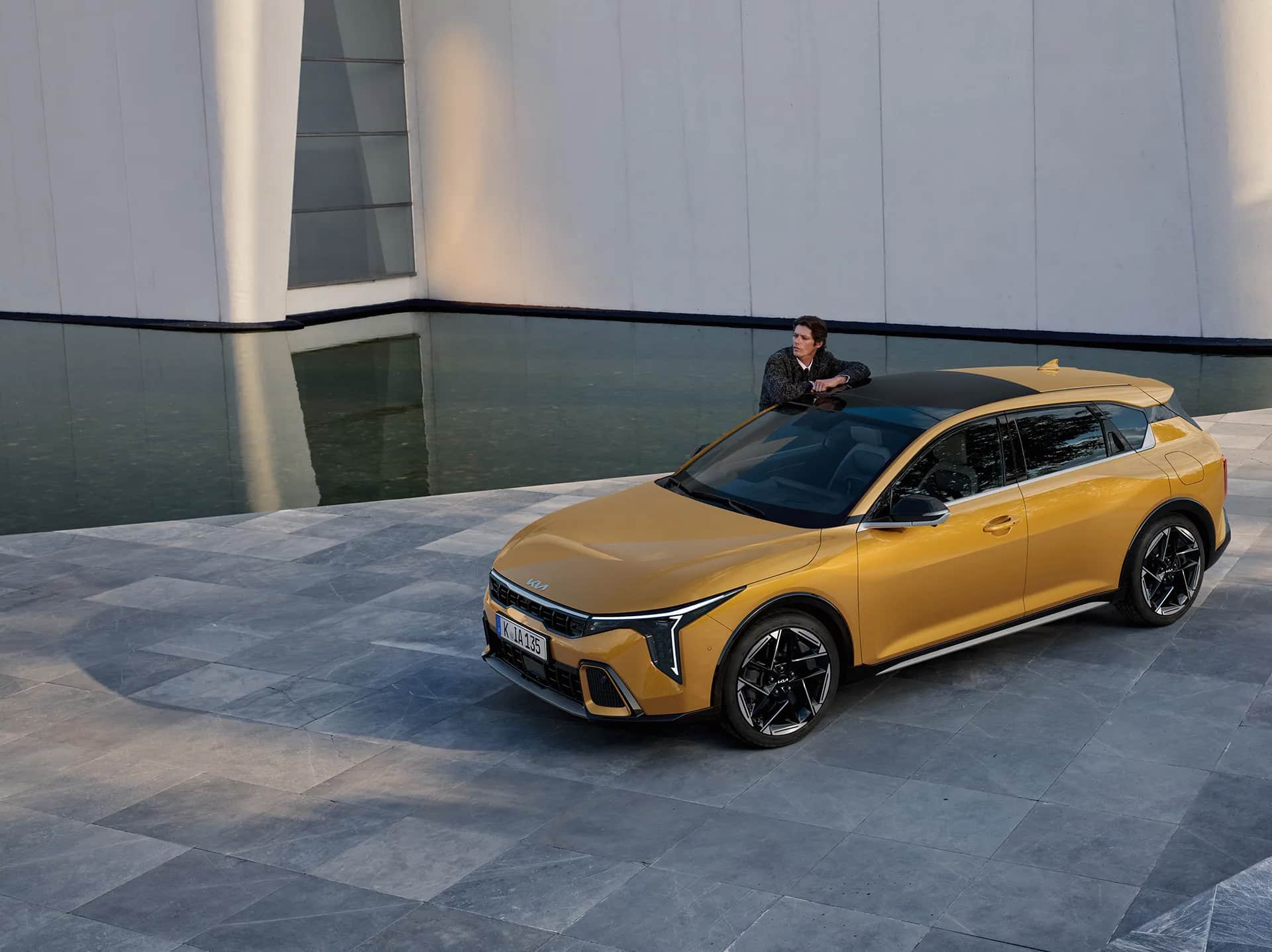Kia K4 steht vor einem Gebäude während ein Mann am Auto lehnt