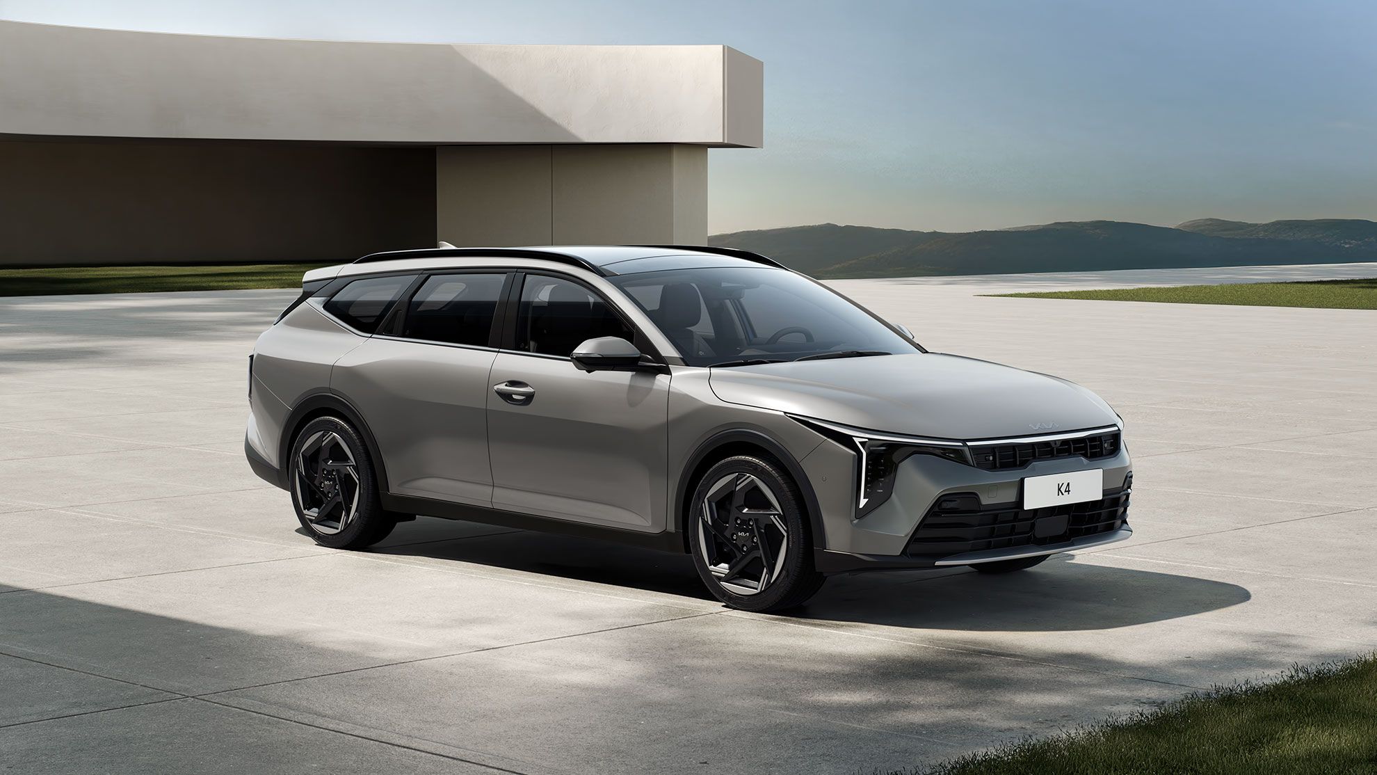 Grauer Kia K4 Sportswagon steht auf einer freien Fläche vor modernem Gebäude und Landschaft im Hintergrund