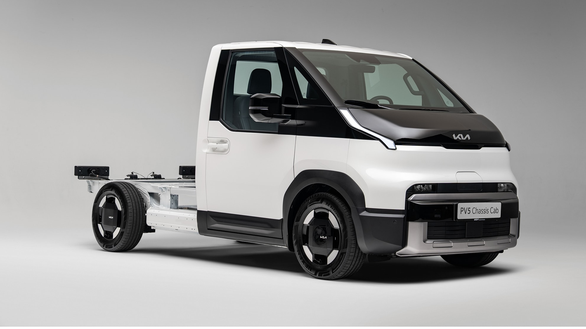 Ein weißer Kia PV5 Chassis Cab Elektro-Transporter als Fahrgestell mit Kabine in der Front-Seitenansicht vor einem neutralen grauen Hintergrund