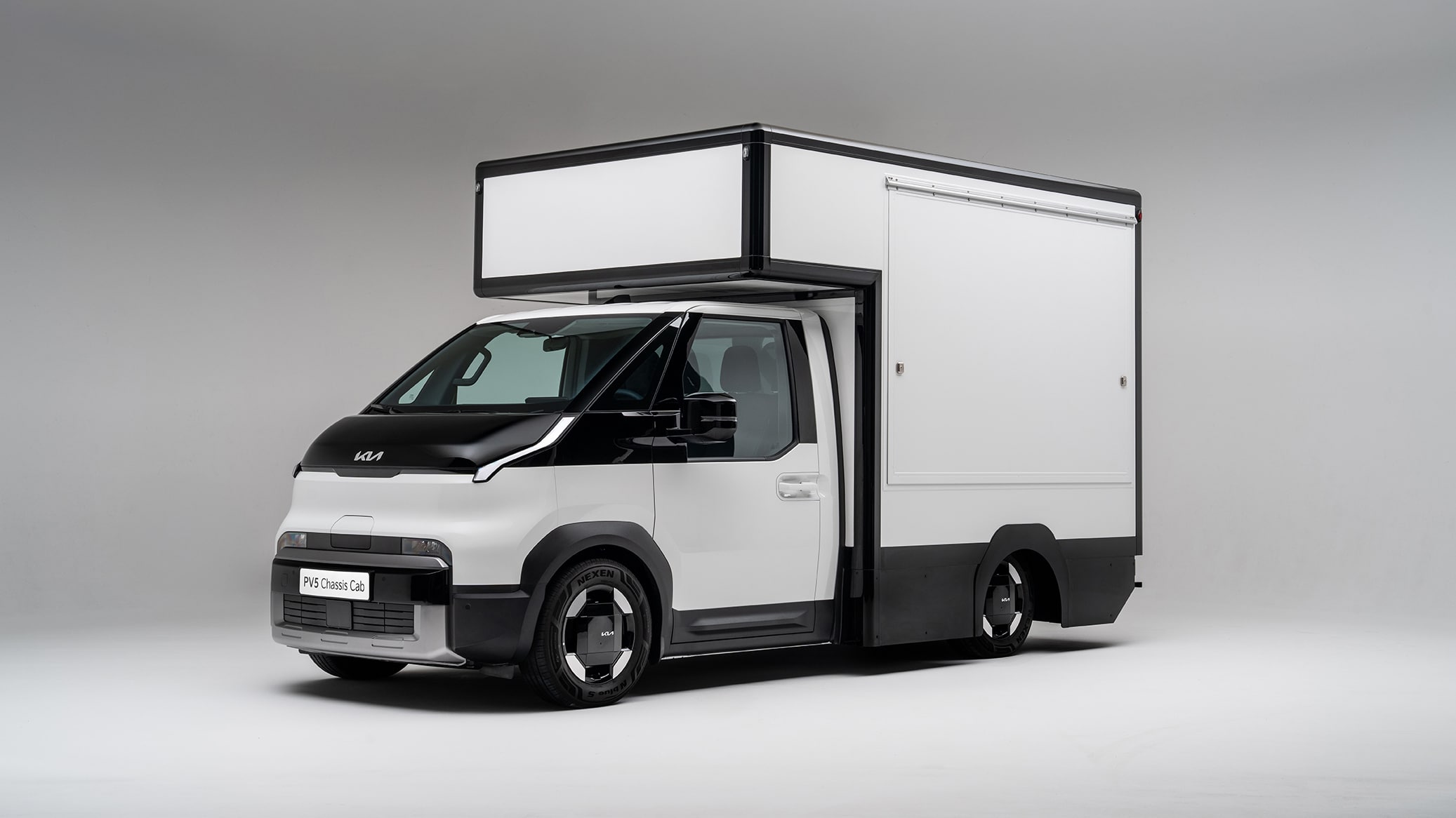 Ein weißer Kia PV5 Chassis Cab Elektro-Transporter mit einem großen, quaderförmigen Kofferaufbau in der Front-Seitenansicht
